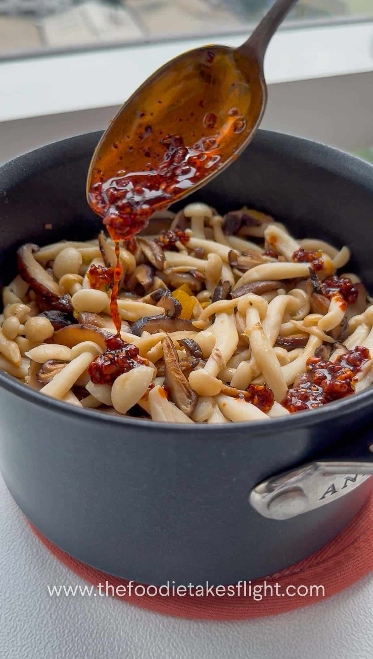 adding chili oil to a pot topped with mushrooms