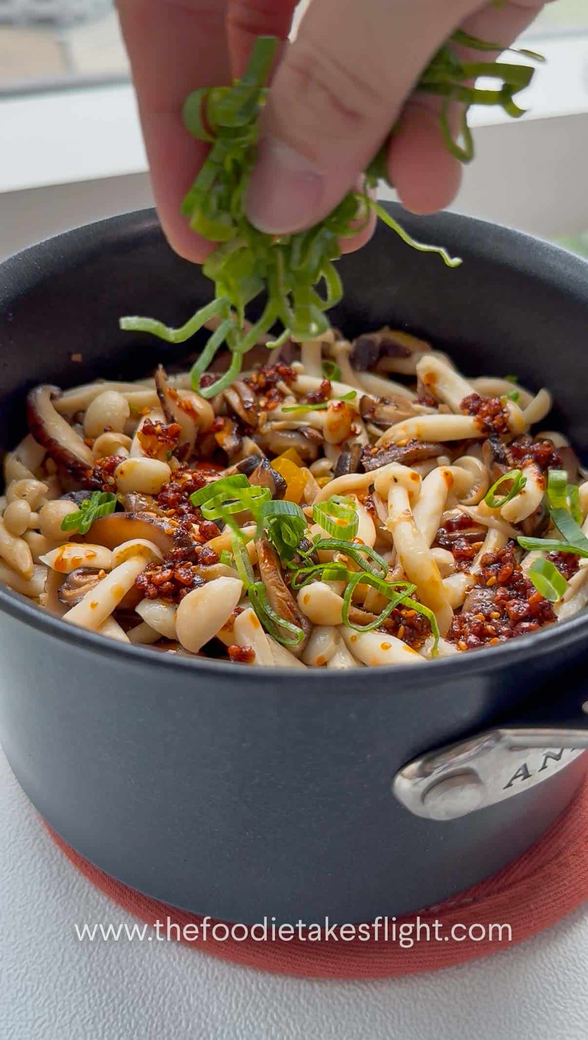 adding chili oil to a pot topped with mushrooms and green onions