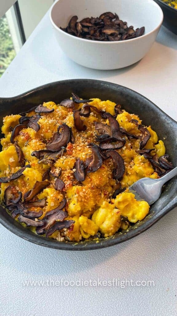 Finished pumpkin miso pasta garnished with chili breadcrumbs and shiitake bacon on a dark grey plate