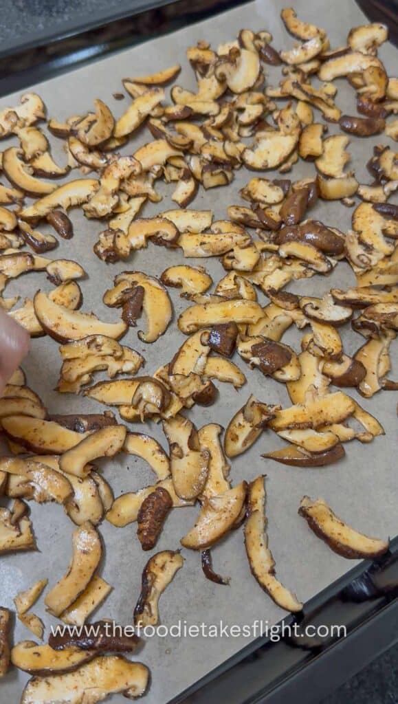Shiitake mushroom slices coated in smoky seasoning on parchment paper ready to bake