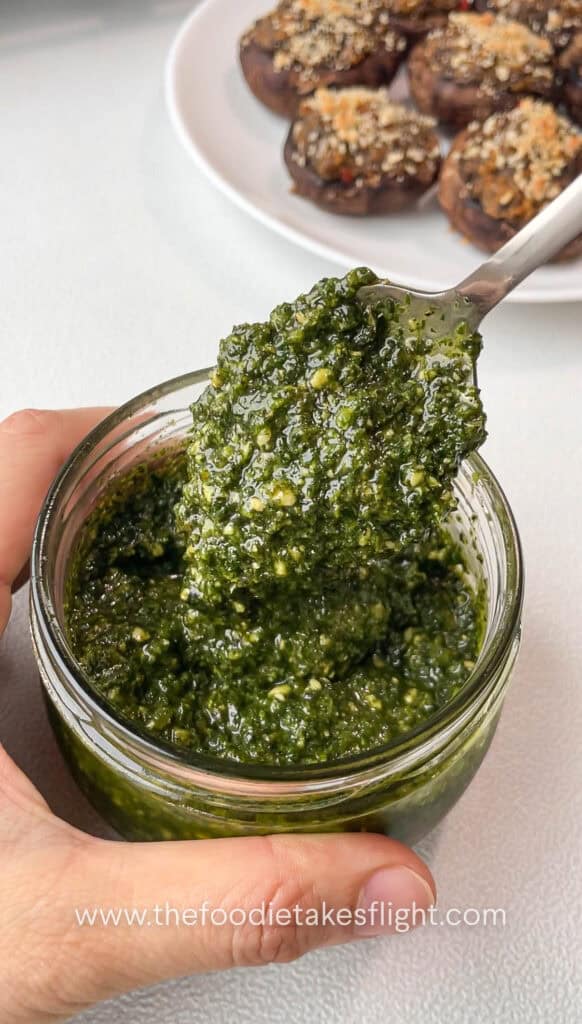 Fresh pesto being added to the center of each stuffed mushroom before serving.