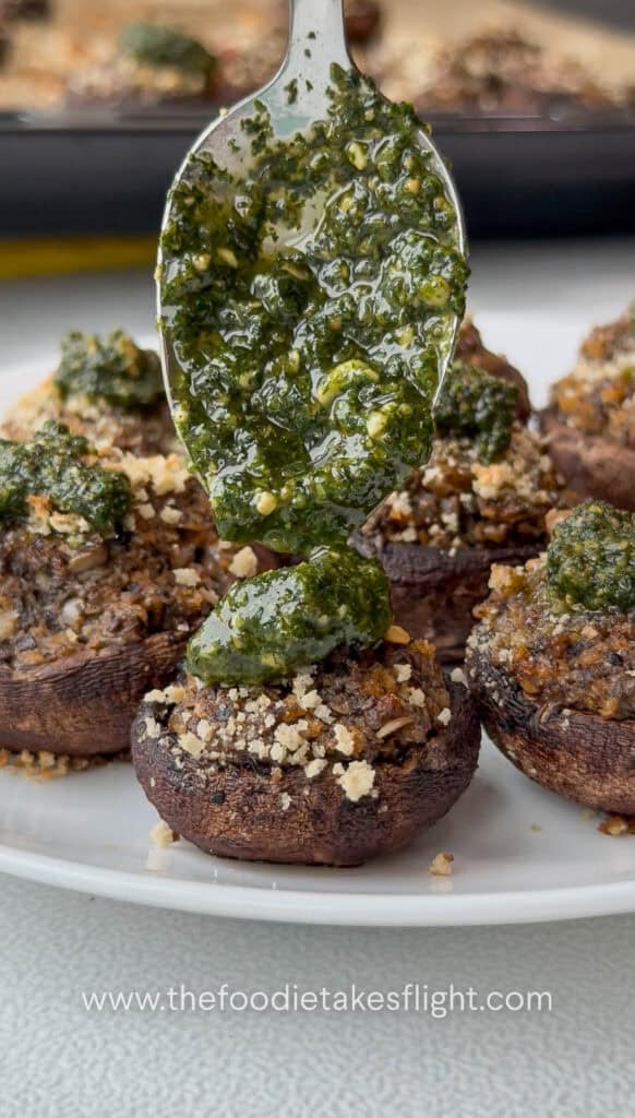 Fresh pesto being added to the center of each stuffed mushroom before serving.
