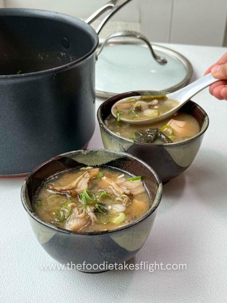 Bowl of maitake mushroom miso soup with soft tofu, wakame, and sliced green onions on top