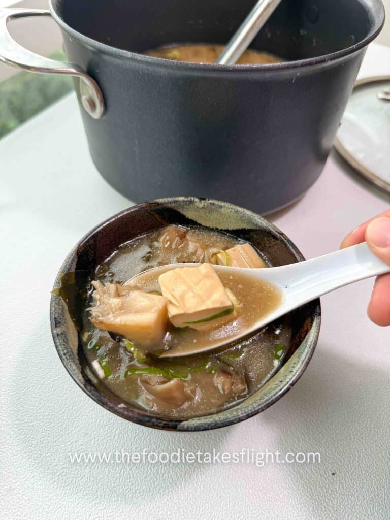 Bowl of maitake mushroom miso soup with soft tofu, wakame, and sliced green onions on top