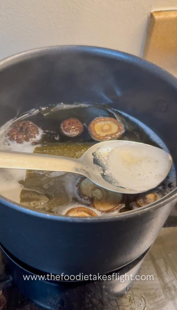 Pot of kombu–shiitake dashi simmering with foam being skimmed from the surface
