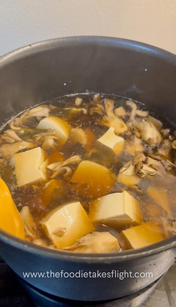 Diced silken tofu being added to the simmering miso soup base