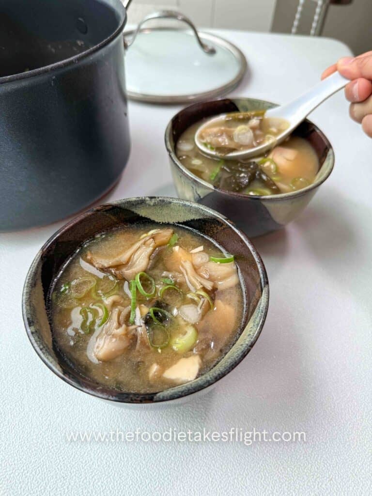 Bowl of maitake mushroom miso soup with soft tofu, wakame, and sliced green onions on top