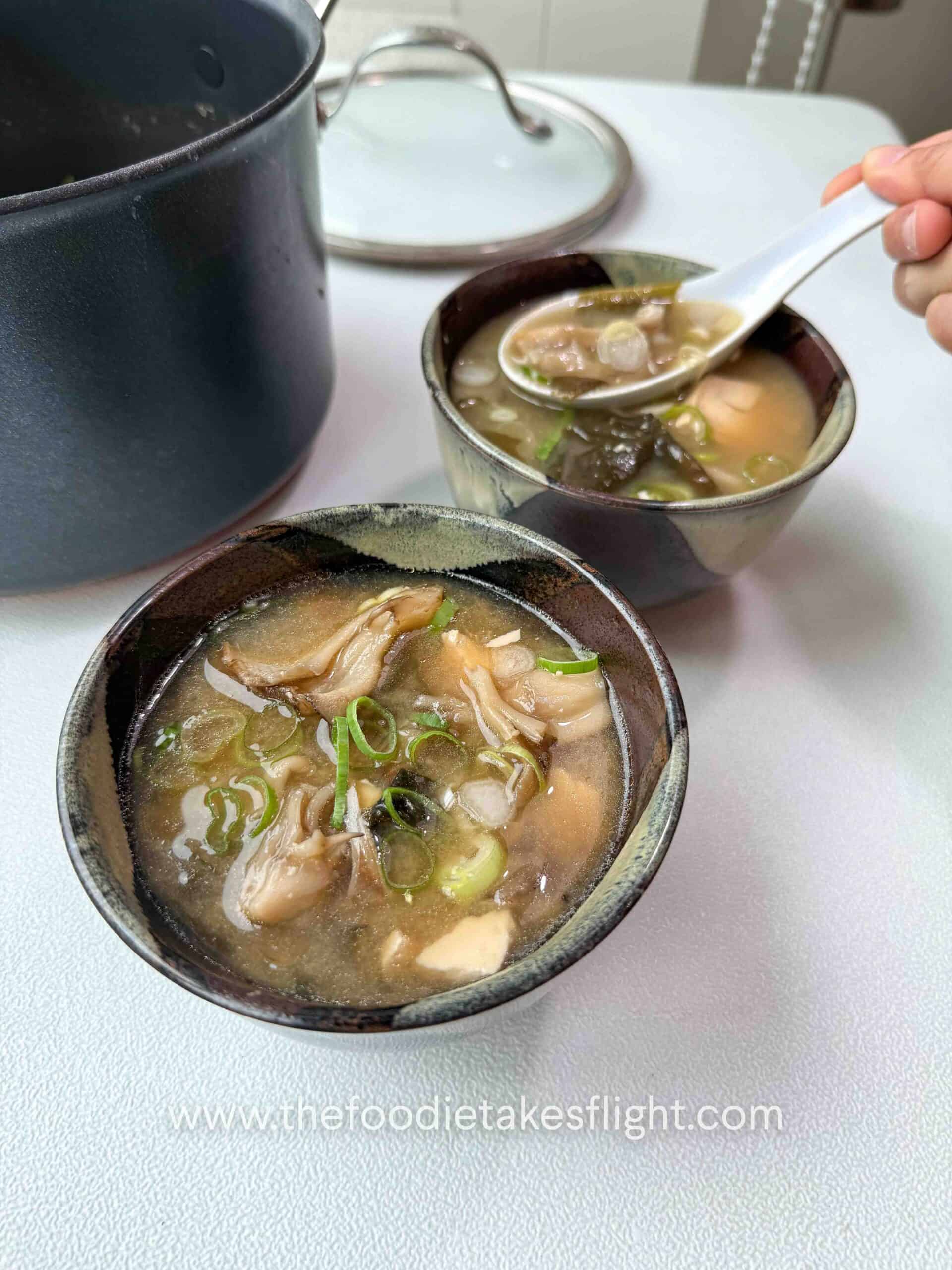 Bowl of maitake mushroom miso soup with soft tofu, wakame, and sliced green onions on top