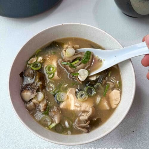 Bowl of maitake mushroom miso soup with soft tofu, wakame, and sliced green onions on top