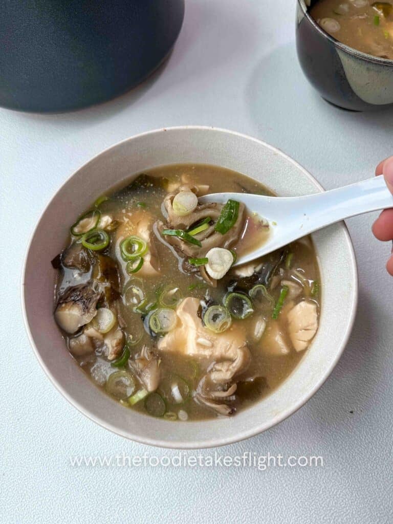 Bowl of maitake mushroom miso soup with soft tofu, wakame, and sliced green onions on top