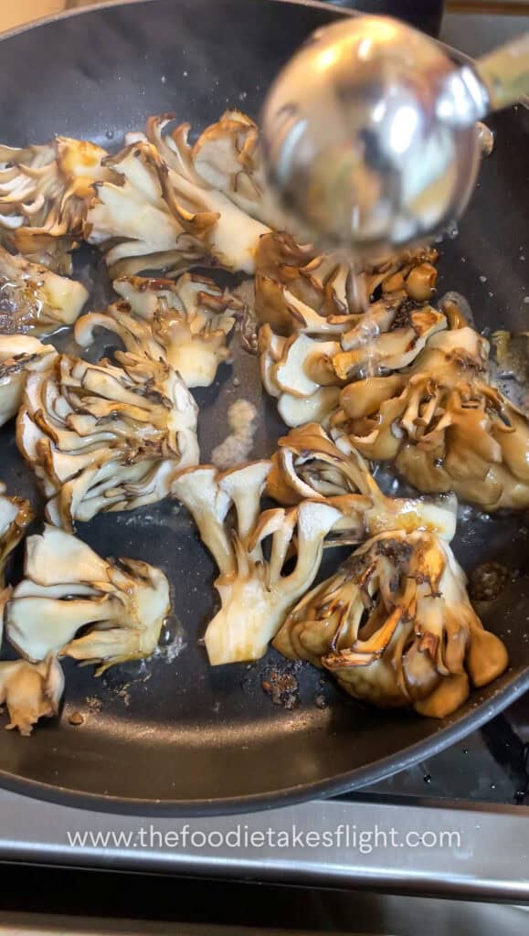 Maitake mushrooms searing in a pan until browned and caramelised with soy sauce and mirin