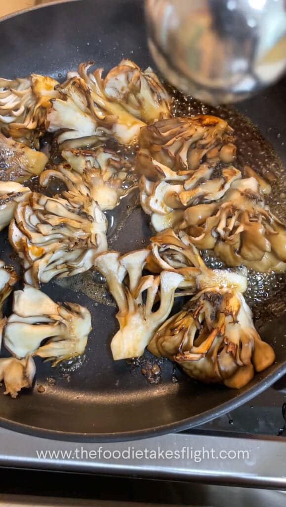 Maitake mushrooms searing in a pan until browned and caramelised with soy sauce and mirin