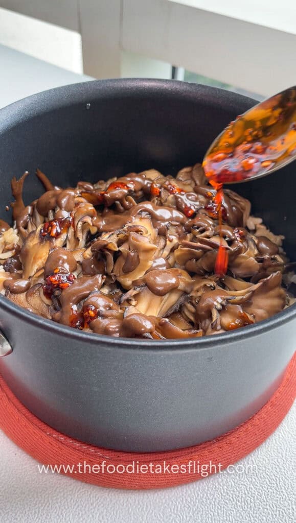 drizzling chili oil on pot of rice topped with maitake mushrooms