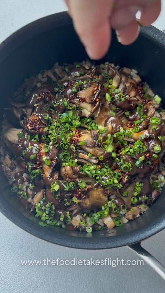adding chives to pot of rice topped with maitake mushrooms