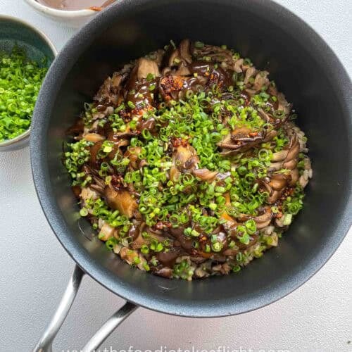 Overhead shot of a rice pot filled with glazed maitake mushrooms, drizzles of black garlic miso sauce and chives