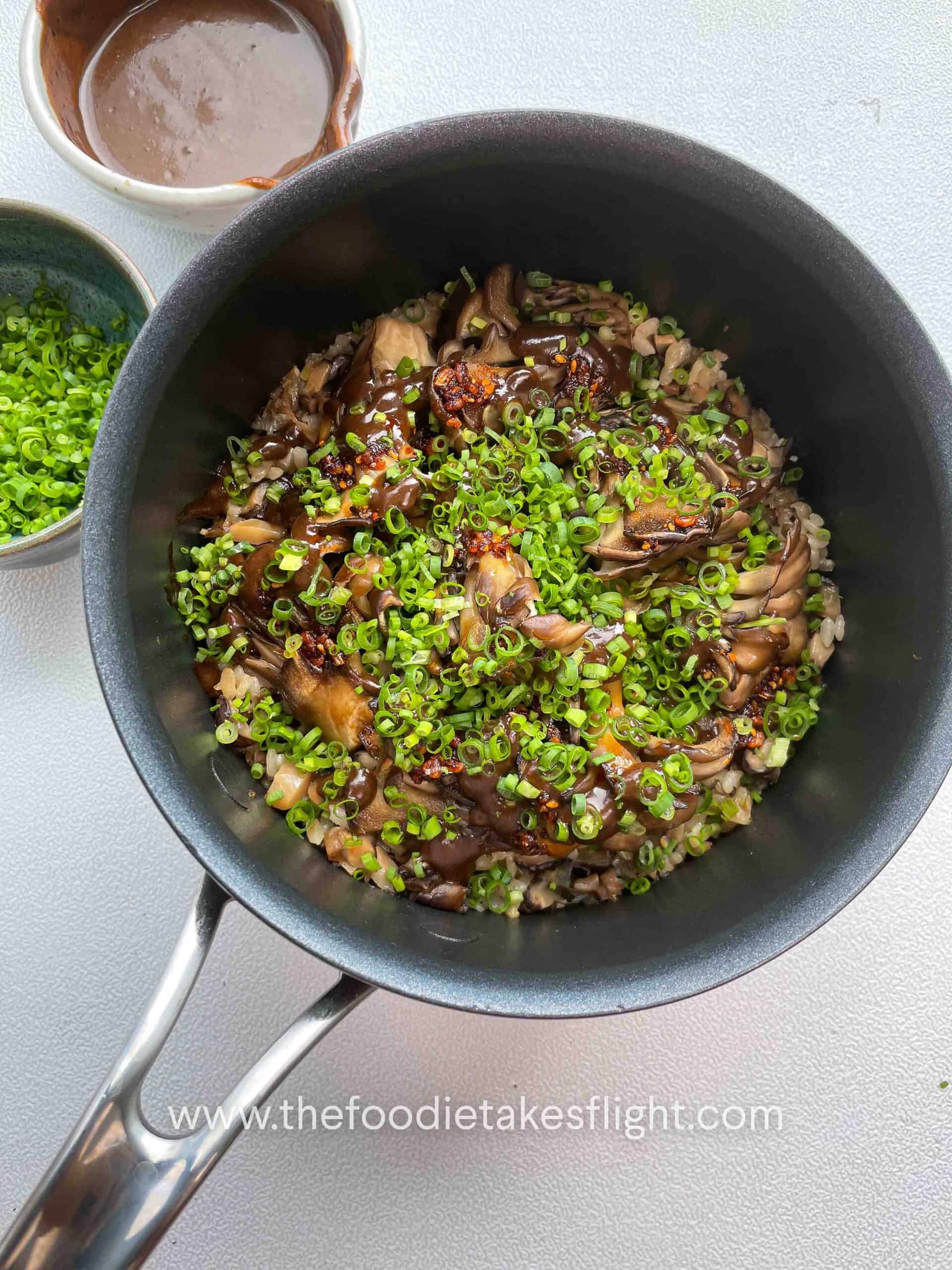 Overhead shot of a rice pot filled with glazed maitake mushrooms, drizzles of black garlic miso sauce and chives