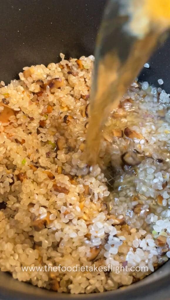 Uncooked short-grain rice being stirred with soy sauce and mirin in a pot
