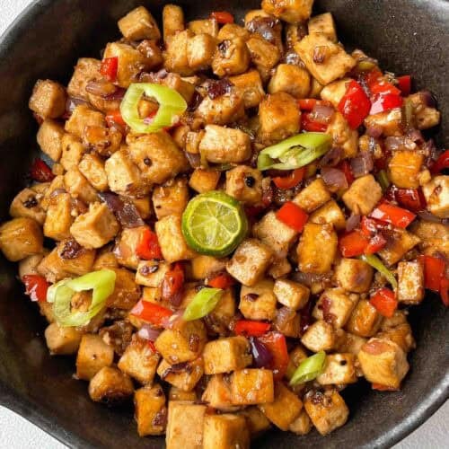 Close-up of saucy tofu cubes coated in vegetarian oyster sauce with chopped chilies on top