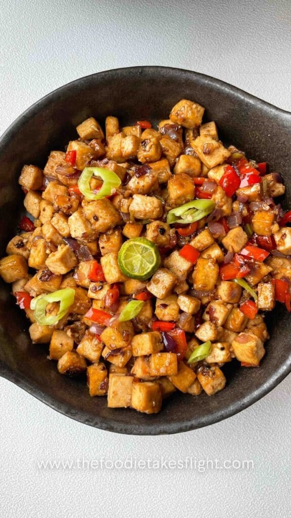 Close-up of saucy tofu cubes coated in vegetarian oyster sauce with chopped chilies on top