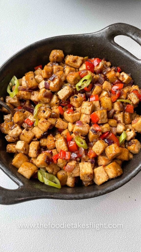 Close-up of saucy tofu cubes coated in vegetarian oyster sauce with chopped chilies on top