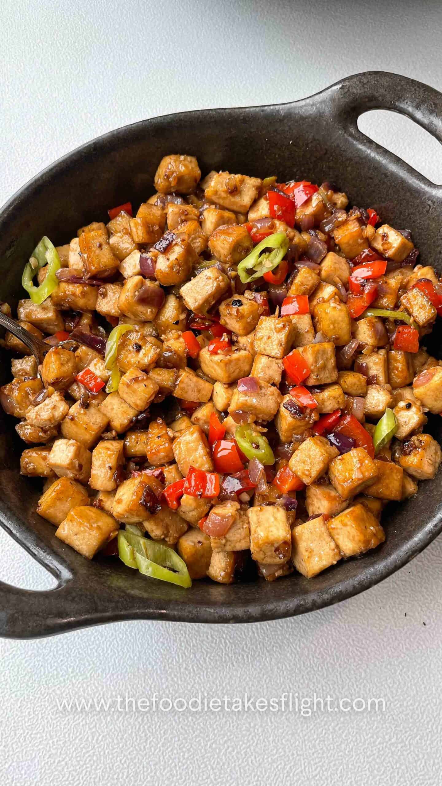 Close-up of saucy tofu cubes coated in vegetarian oyster sauce with chopped chilies on top