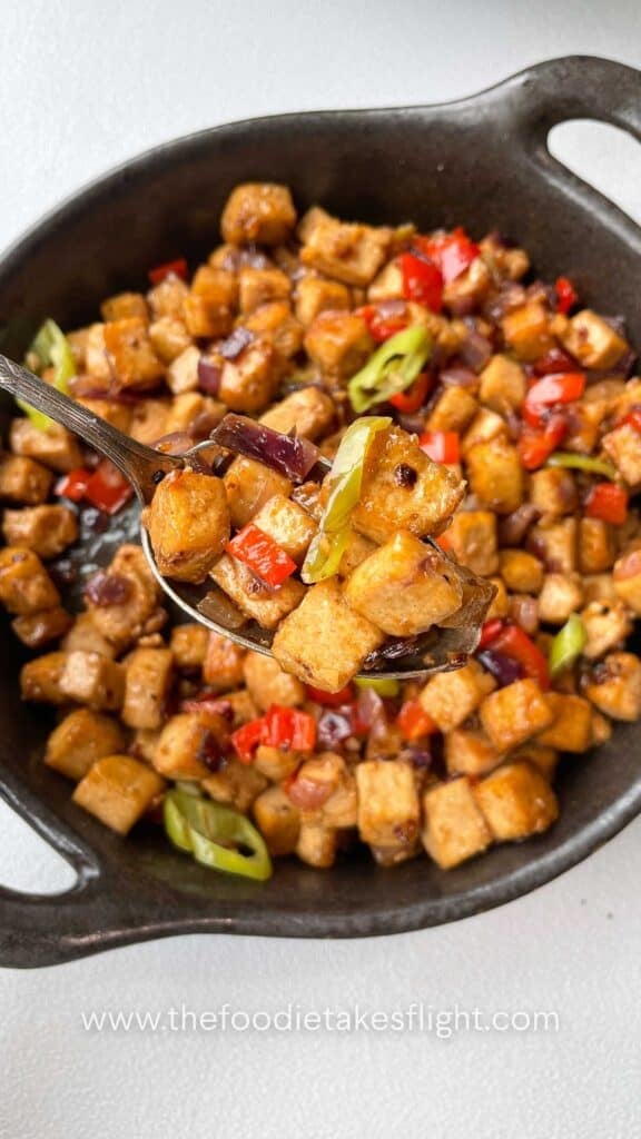Close-up of saucy tofu cubes coated in vegetarian oyster sauce with chopped chilies on top