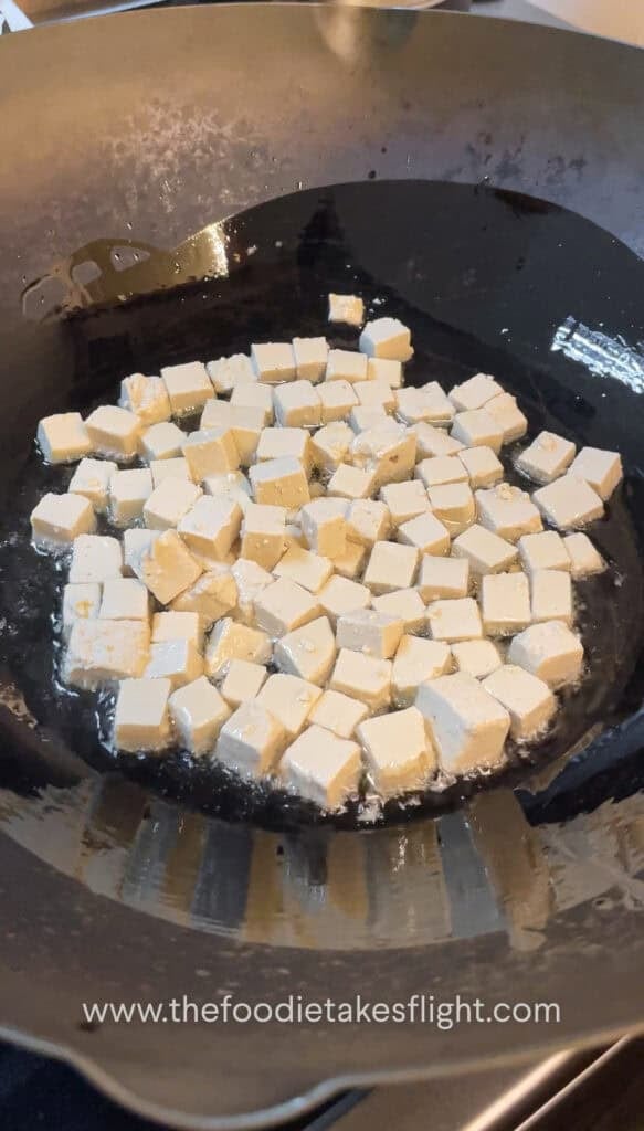 Cubed tofu frying in a wok until golden and crisp