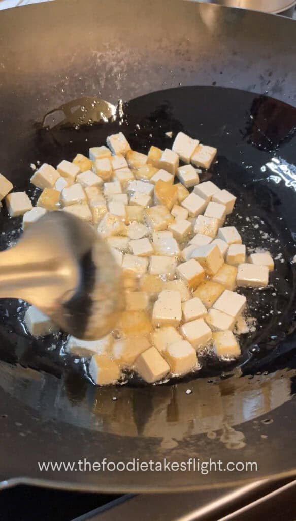 Cubed tofu frying in a wok until golden and crisp
