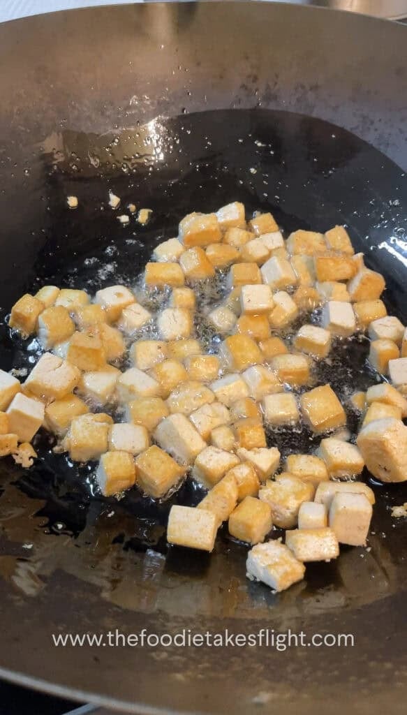 Cubed tofu frying in a wok until golden and crisp