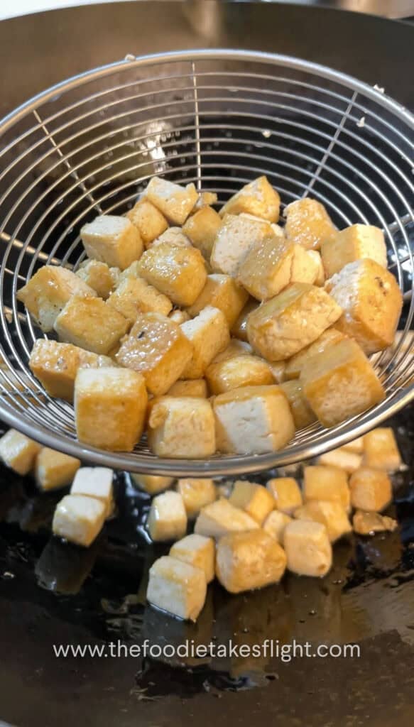 golden brown cubes of tofu fried in a wok