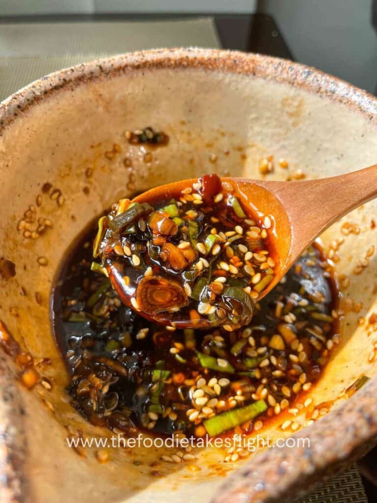 Small bowl of sweet and spicy all-around dipping sauce with visible garlic, scallions, and chili oil
