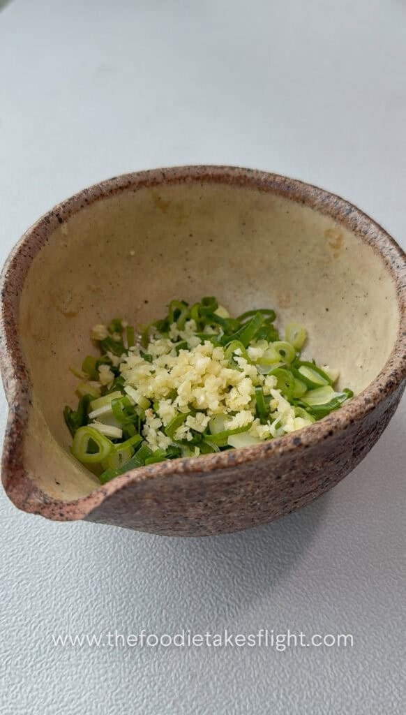 Pouring hot oil over garlic and green onions to bloom aromatics for dipping sauce