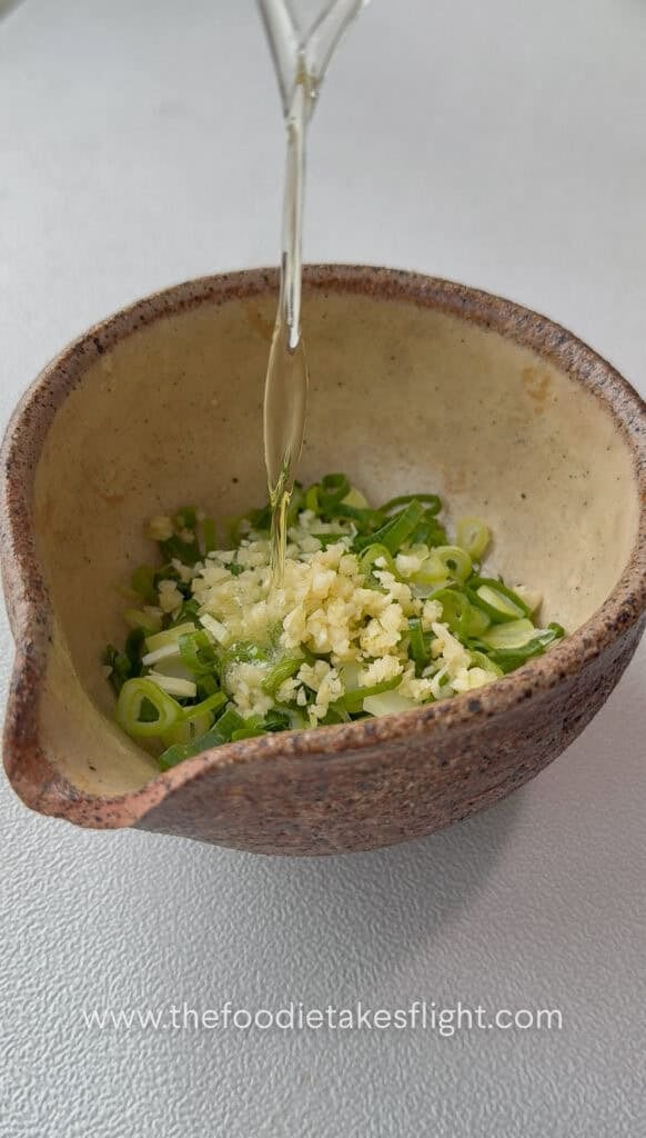 Pouring hot oil over garlic and green onions to bloom aromatics for dipping sauce