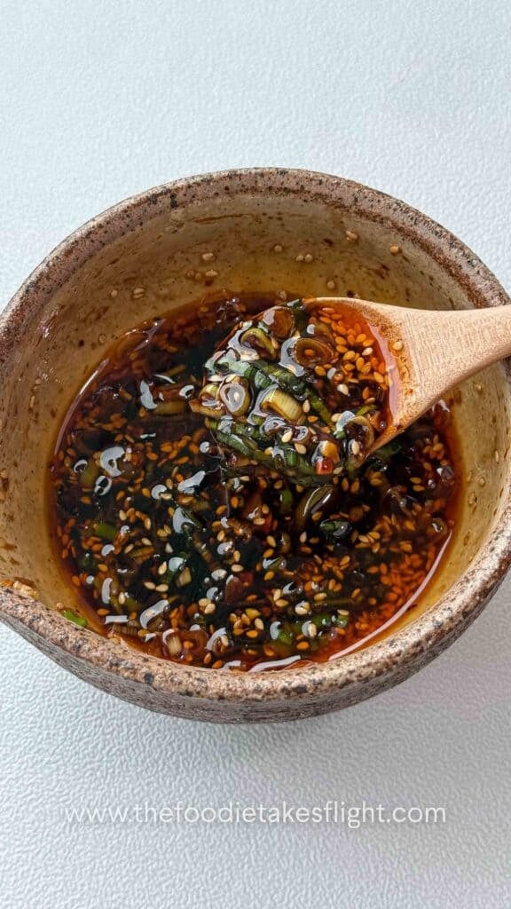 Small bowl of sweet and spicy all-around dipping sauce with visible garlic, scallions, and chili oil