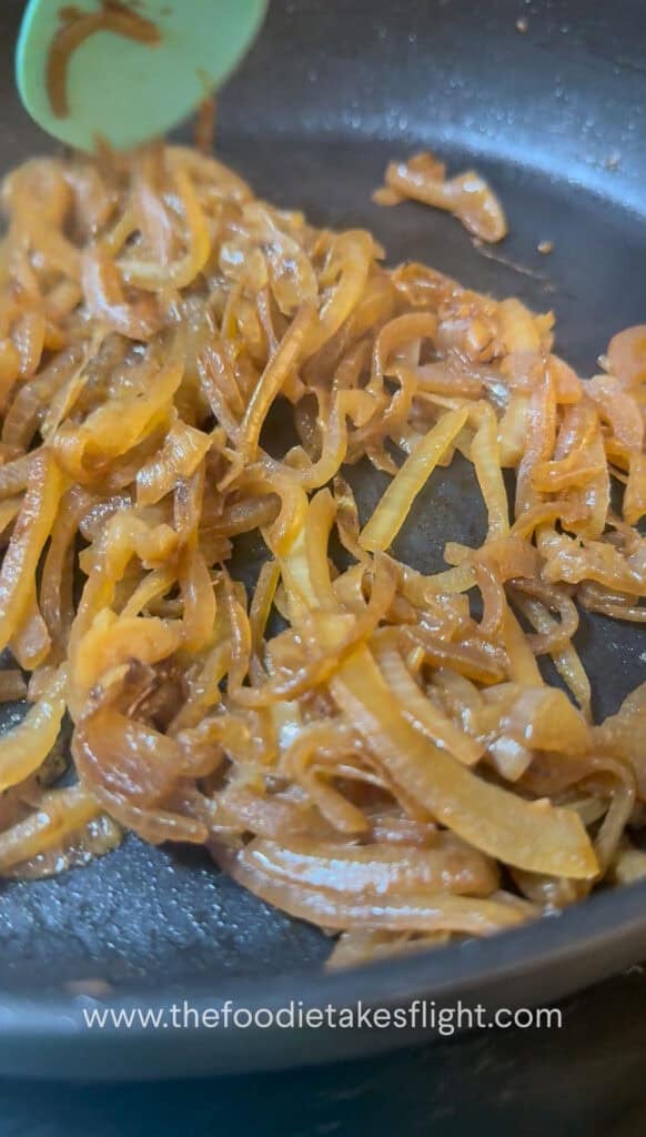 Thinly sliced onions caramelising in a skillet until deep golden brown