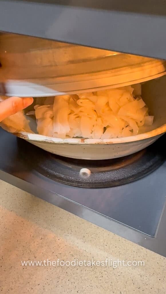 Fresh flat rice noodles being microwaved with a splash of water to loosen them