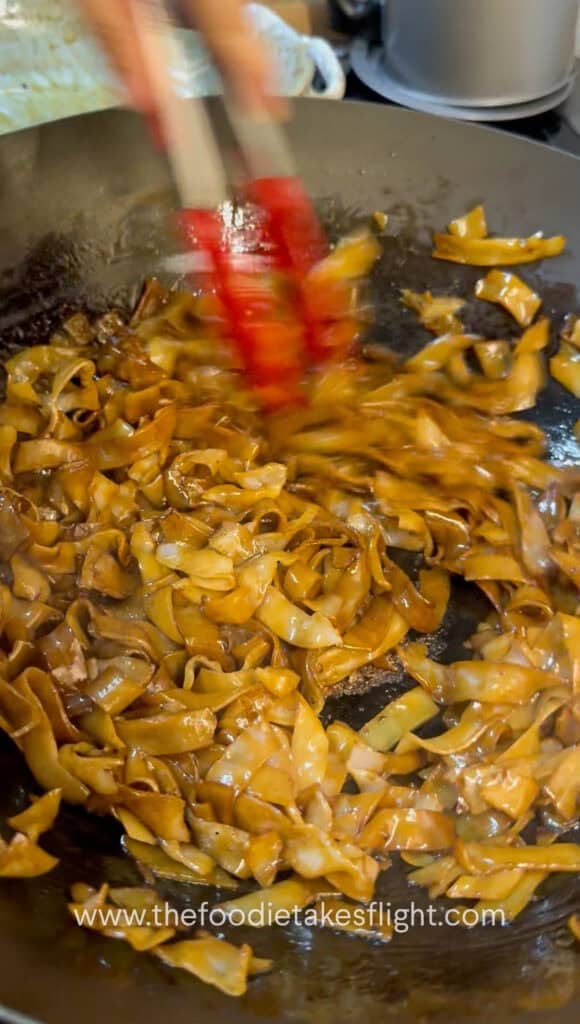 Soy-coated rice noodles caramelizing and lightly charring in a hot wok