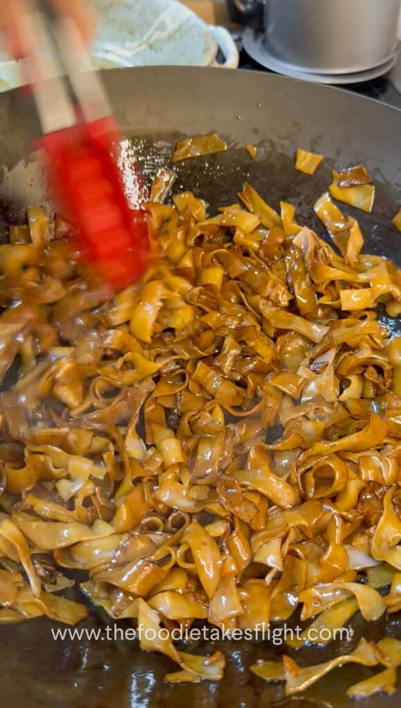 Soy-coated rice noodles caramelizing and lightly charring in a hot wok