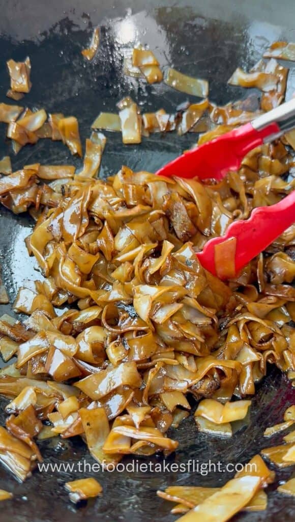 Soy-coated rice noodles caramelizing and lightly charring in a hot wok