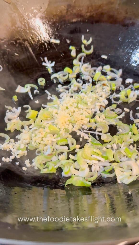 Garlic and green onions sautéing in a wok with oil