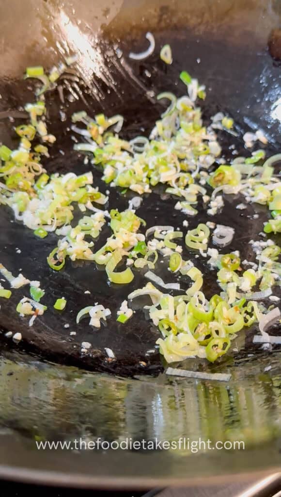 Garlic and green onions sautéing in a wok with oil
