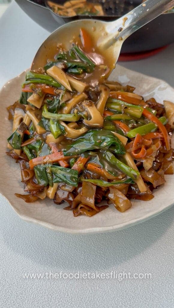 Gravy being poured over stir-fried hor fun noodles before serving