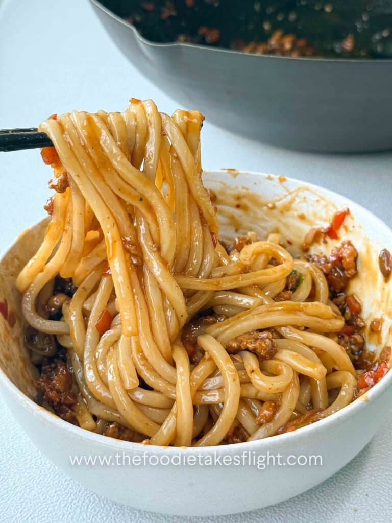 Bowl of calamansi udon noodles tossed in glossy soy citrus sauce with crumbled tofu and peppers