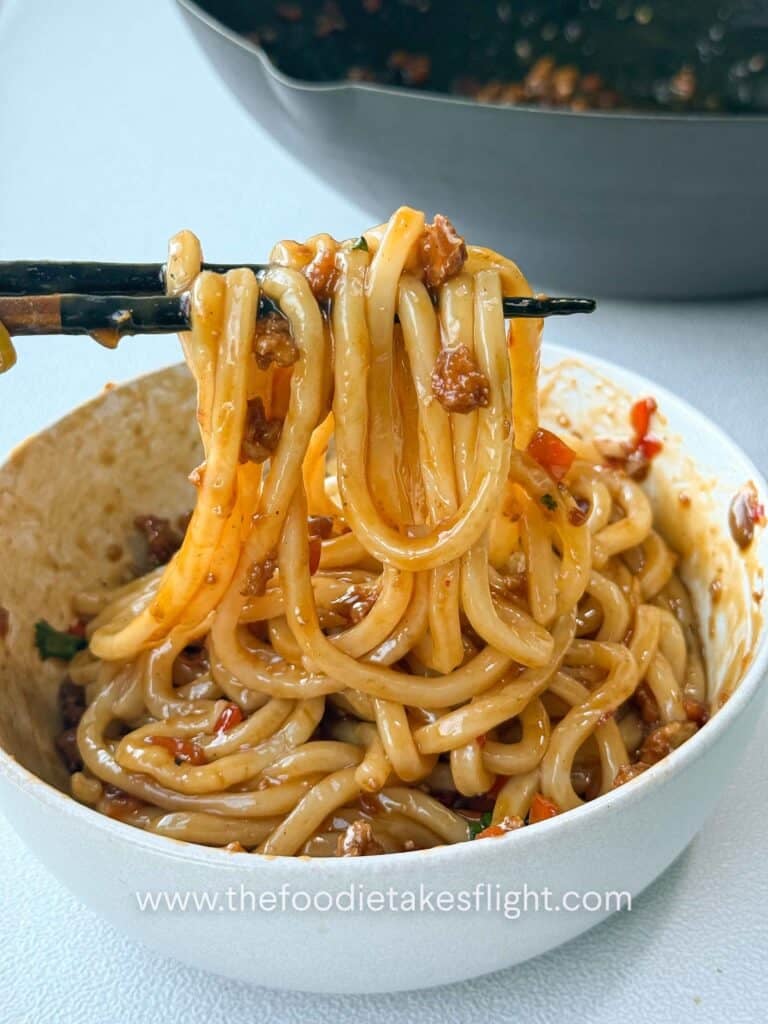 Bowl of calamansi udon noodles tossed in glossy soy citrus sauce with crumbled tofu and peppers