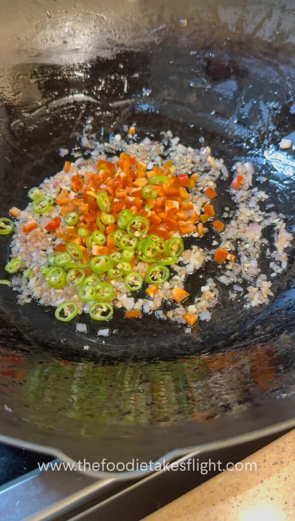 Sliced onions, bell peppers, and green chili stir-frying in a pan