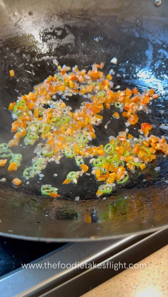 Sliced onions, bell peppers, and green chili stir-frying in a pan