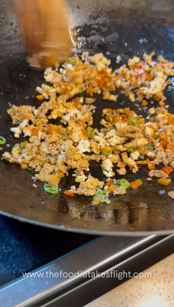 Sliced onions, bell peppers, and green chili with crumbled tofu stir-frying in a pan