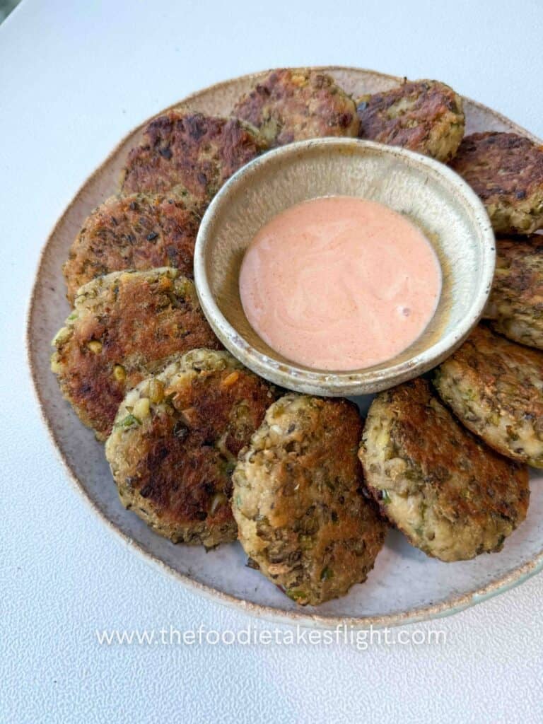Plate of golden pan-fried mung bean patties served with dipping sauce on the side