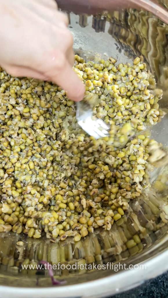 Cooked mung beans being mashed in a bowl with a fork