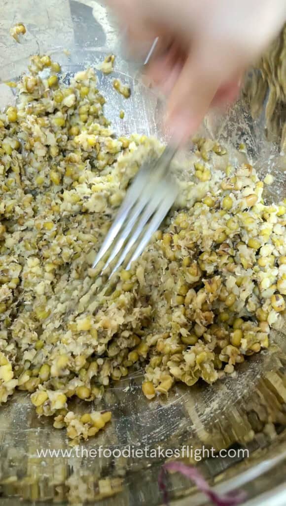 Cooked mung beans being mashed in a bowl with a fork